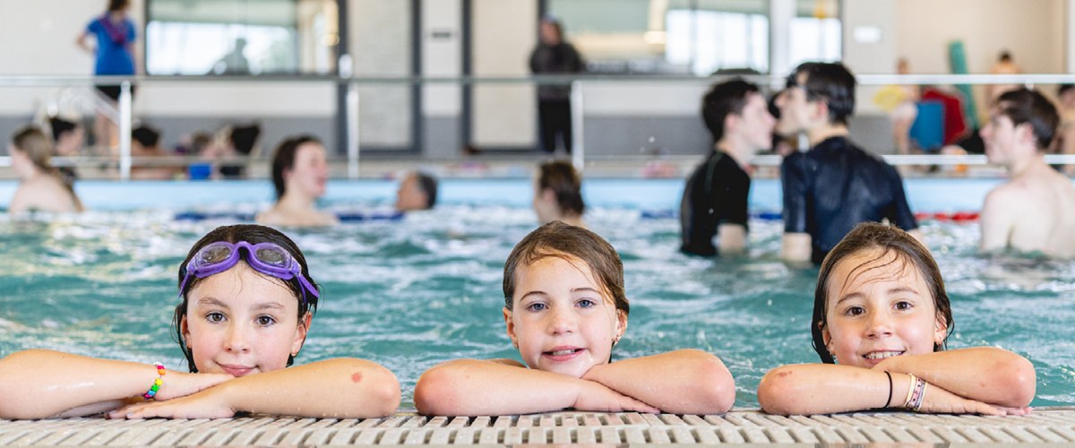 photo of three girls leaning against side of pool.